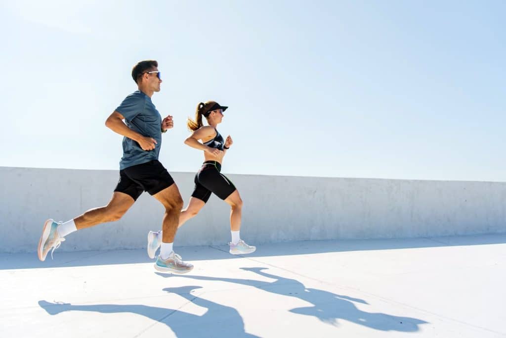A man and woman running together on pavement on a sunny day