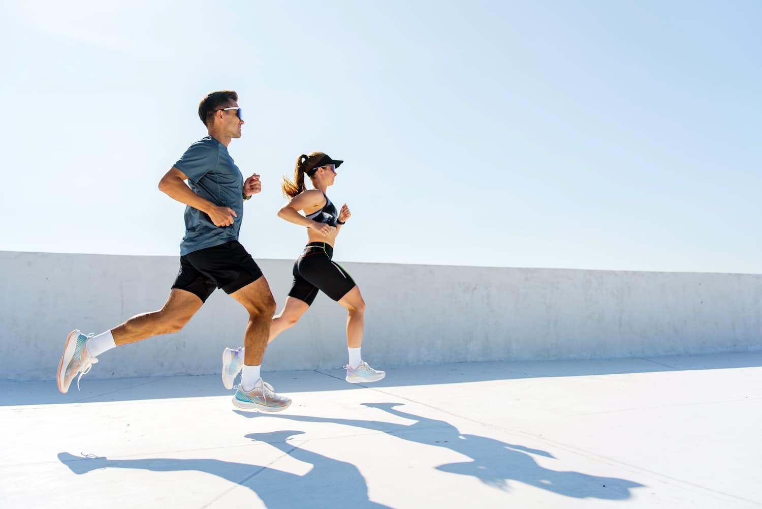 A man and woman running together on pavement on a sunny day