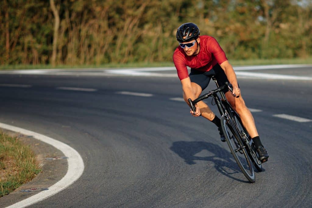 Man wearing sport clothing, protective helmet and mirrored glasses, cycling down a road.