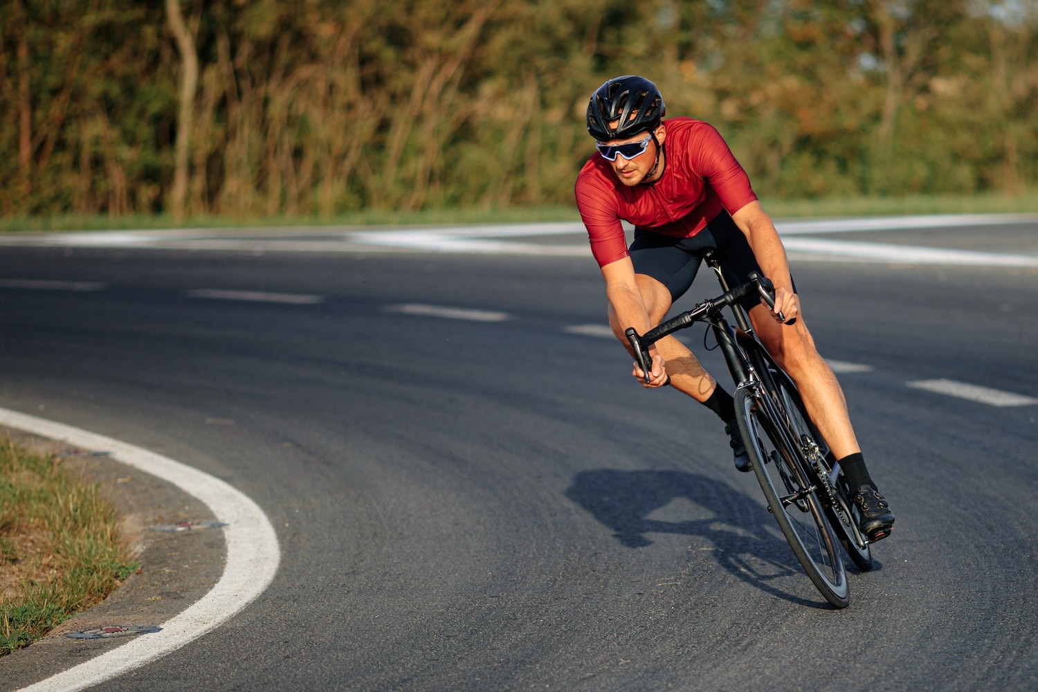 Man wearing sport clothing, protective helmet and mirrored glasses, cycling down a road.