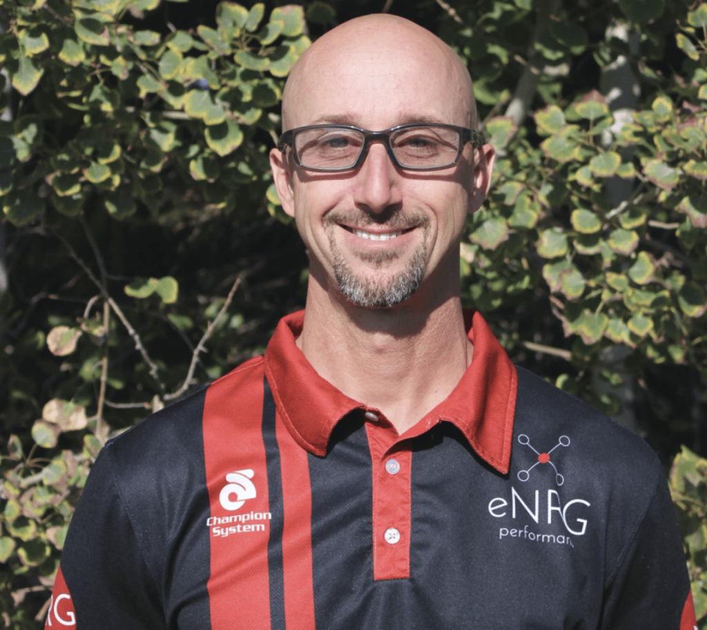 bob smiling with trees in the background, he is wearing a black and red shit with Champion System logo