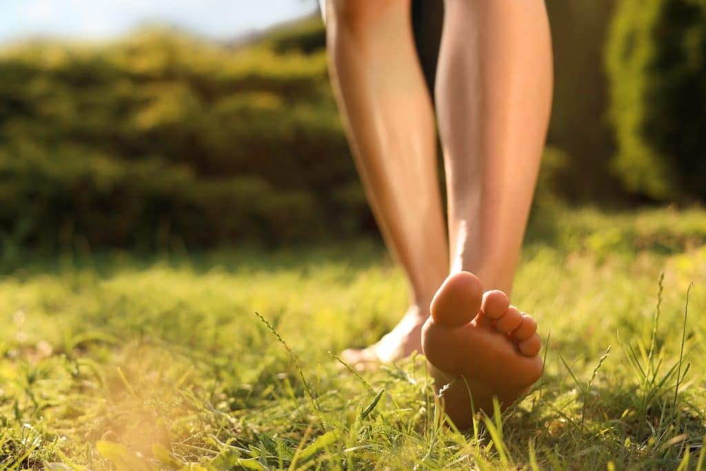 Woman walking barefoot on green grass outdoors, closeup of her feet