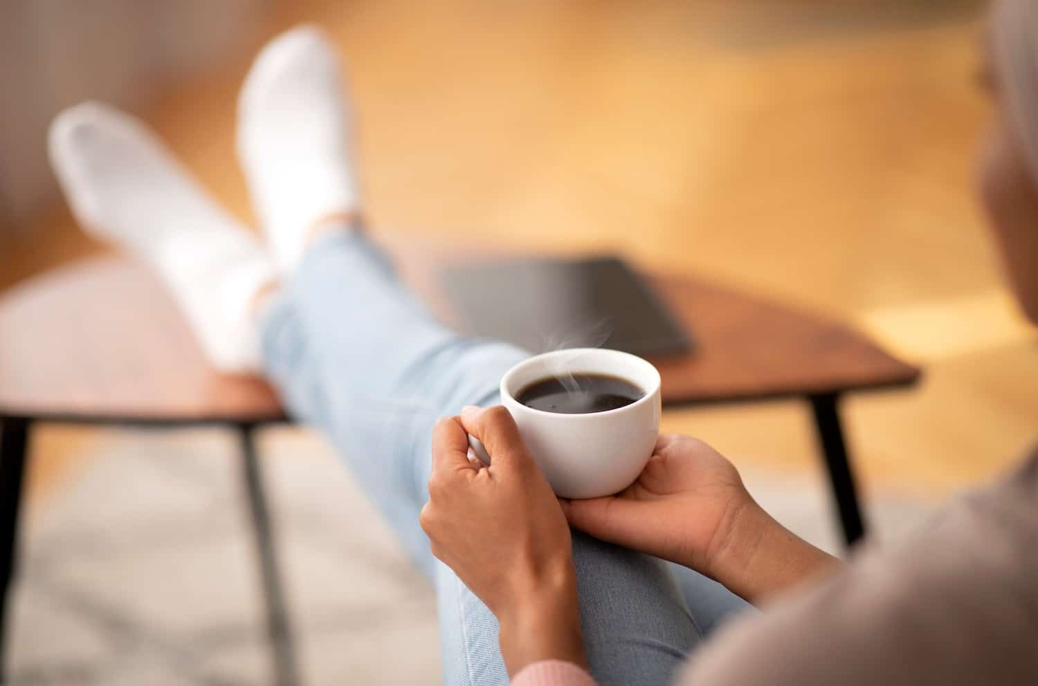 A person holding a cup of coffee with legs crossed and propped on a coffee table