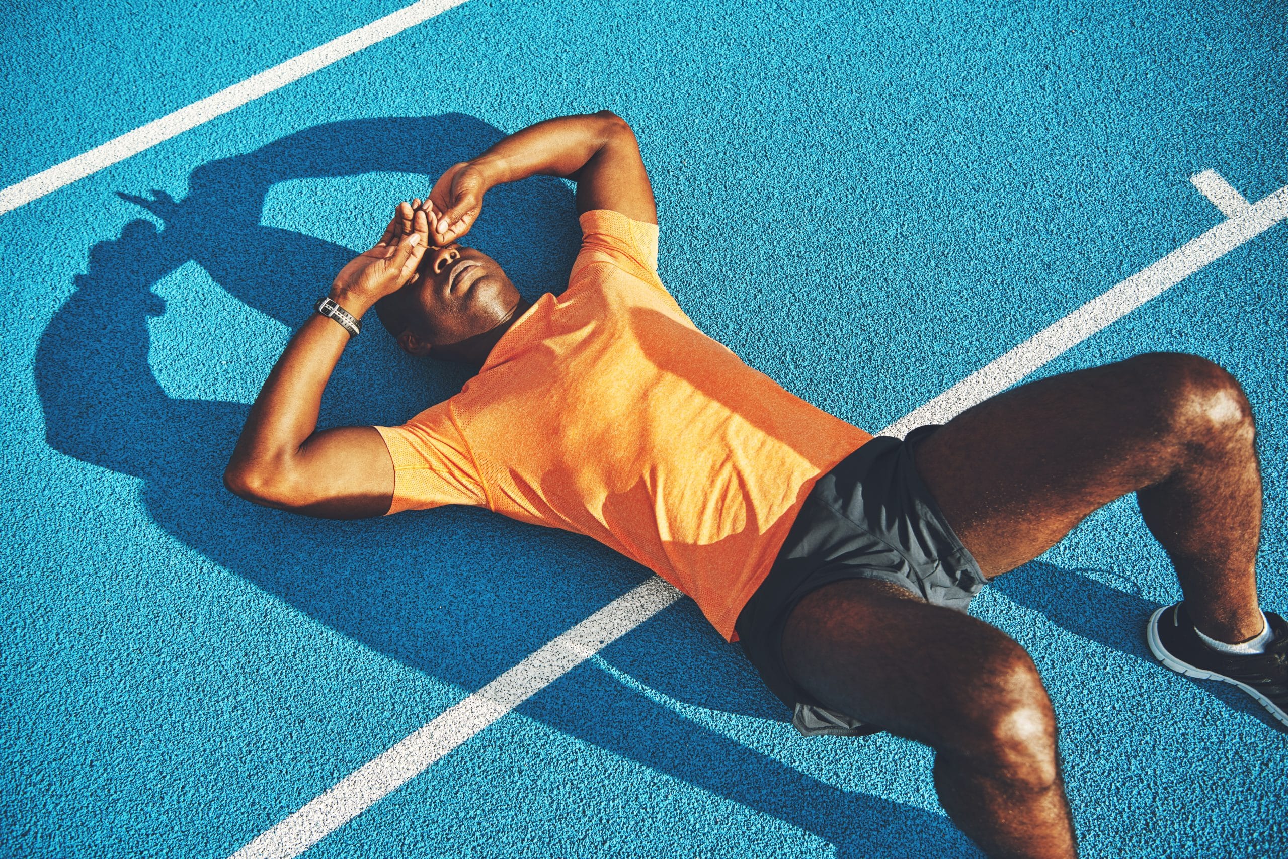 Tired runner lying on a blue track with his hands over his eyes