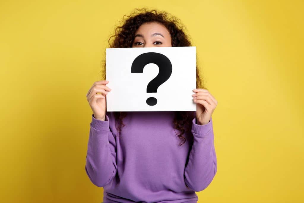 A woman holding a paper with a question mark on it in front of her face