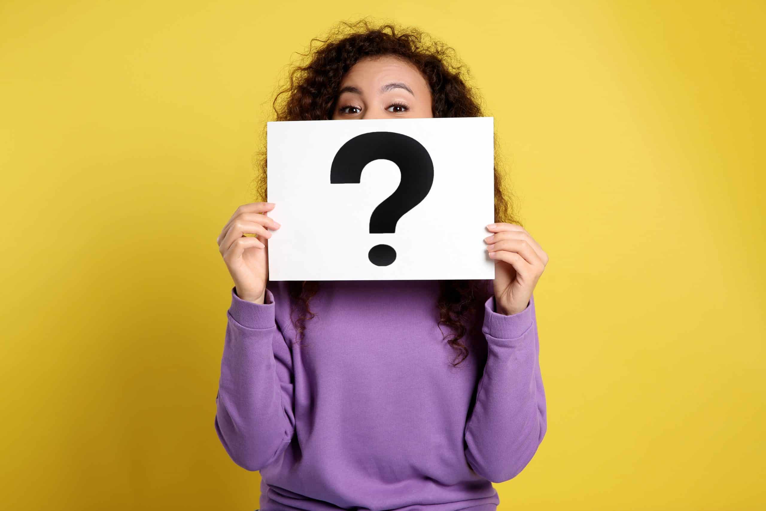 A woman holding a paper with a question mark on it in front of her face
