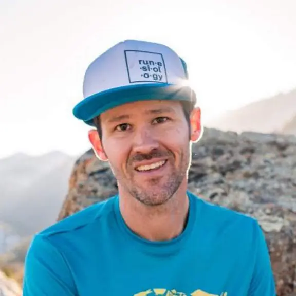 nat smiling wearing a white ball cap and blue shirt with mountains in the background