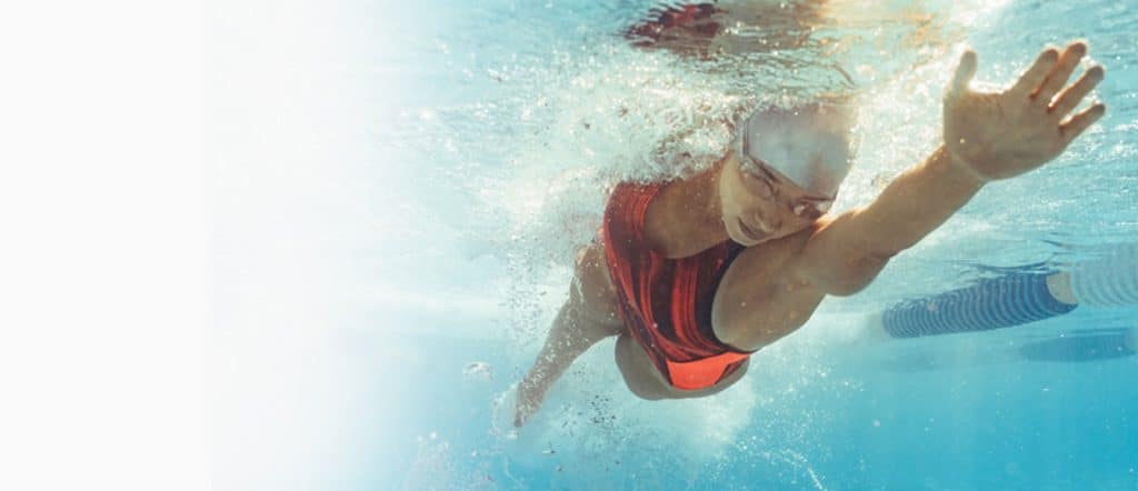 a woman swilling with an orange swimsuit, white cap and googles