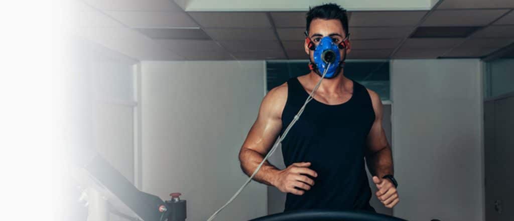 a man in a black tank top running on a treadmill wearing a blue mask