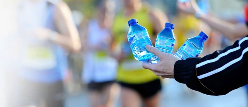 persons hand holding 3 bottles of water and runners in the distance