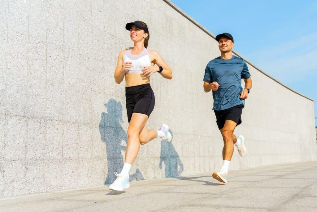 Two runners jog along a modern urban pathway on a sunny day
