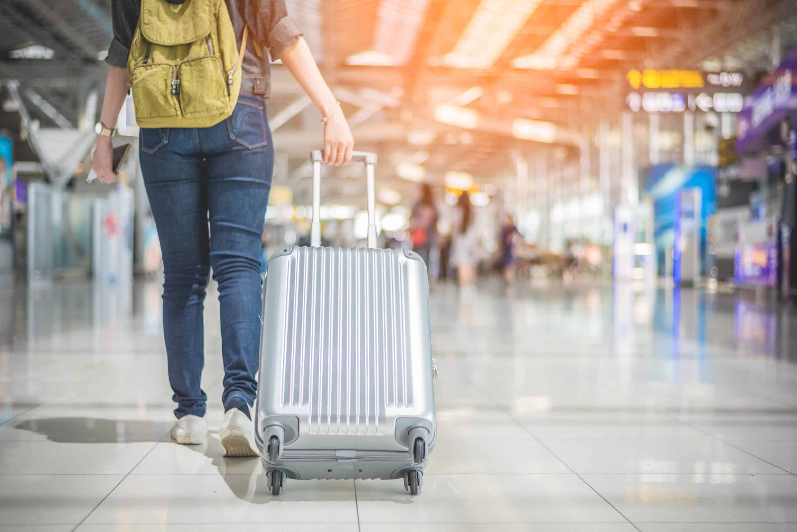 A woman walking through an airport with a backpack on and rolling a silver suitcase