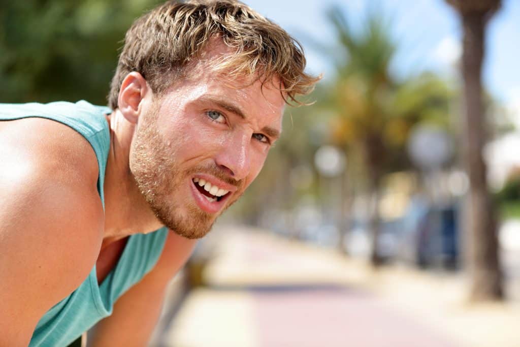 A male runner sweating outside on a sidewalk with palm trees in the background