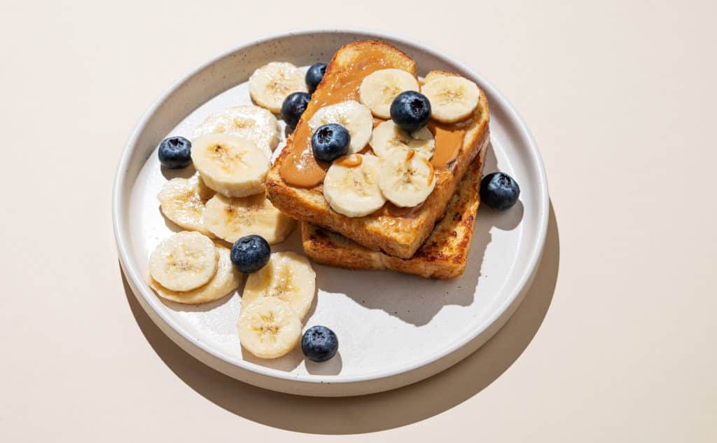 Toast with peanut butter, banana slices, and blueberries on a plate
