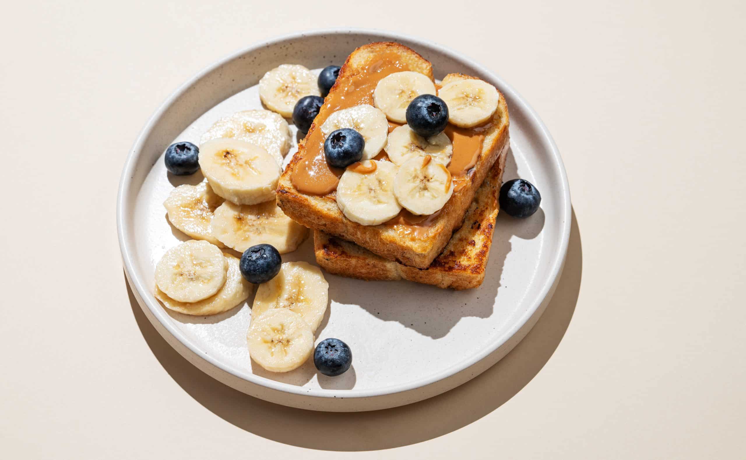 Toast with peanut butter, banana slices, and blueberries on a plate