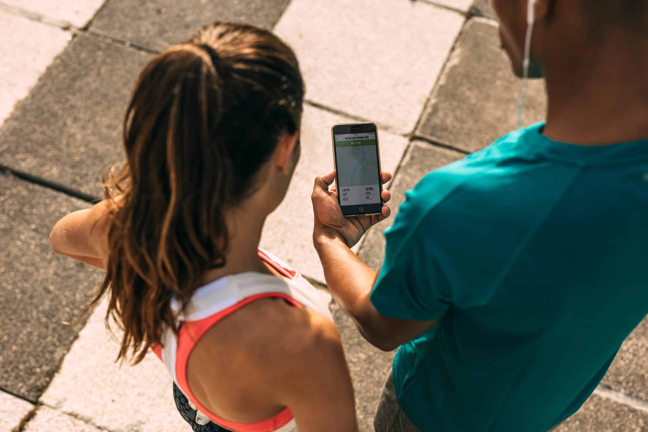 Two runners outside standing on a sidewalk and looking at an app smartphone