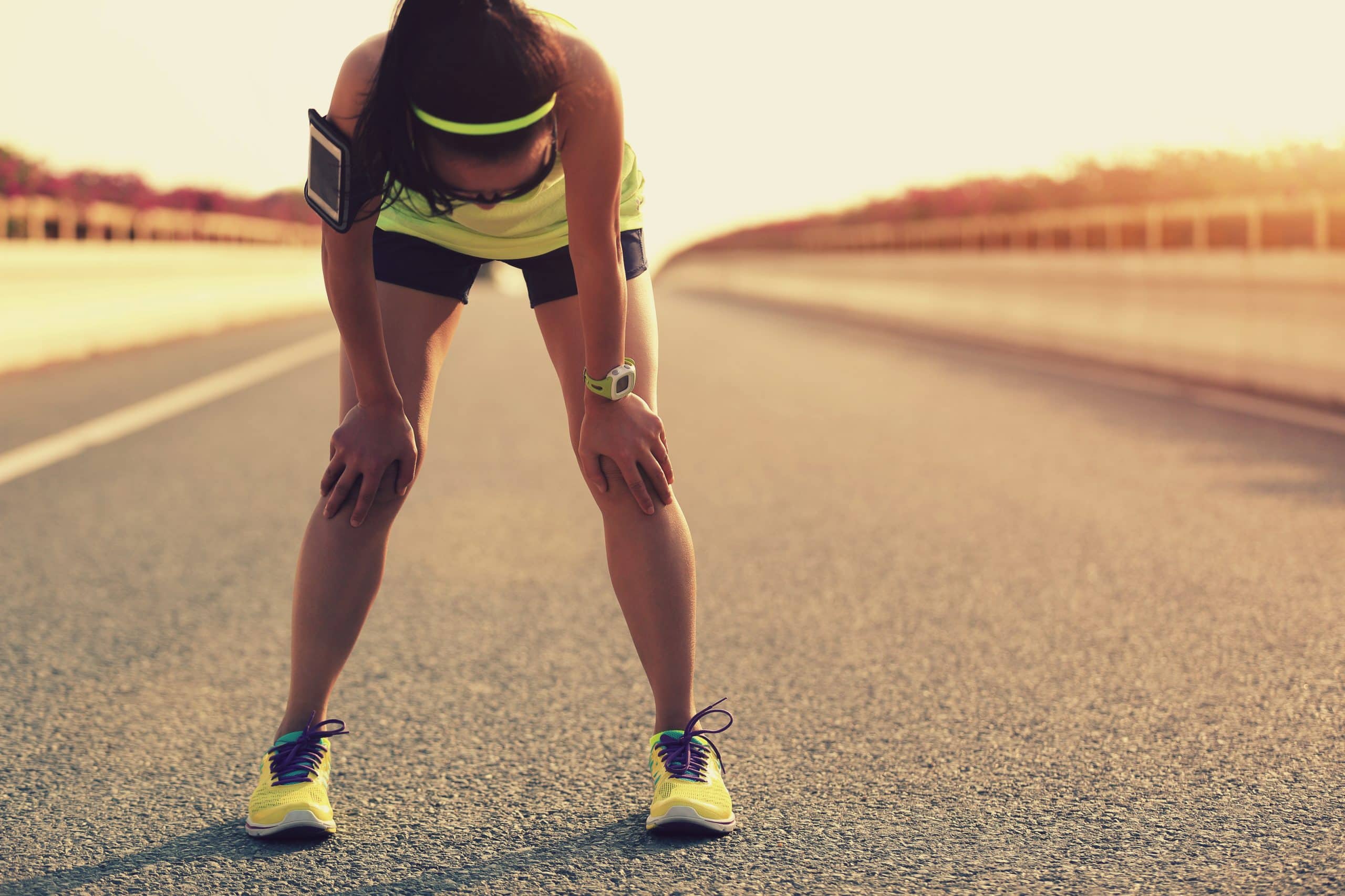 A female runner stopped on a long road, bending over to catch her breath