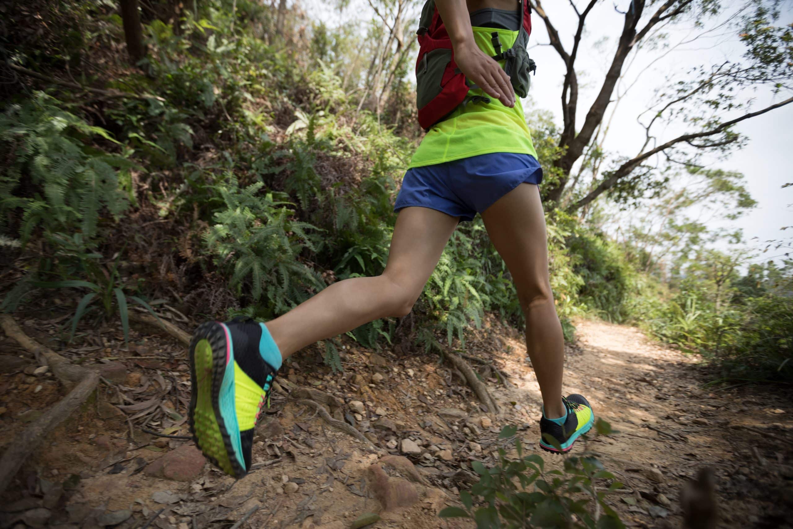 A runner with blue shorts and a neon yellow shirt running on a dirt trail