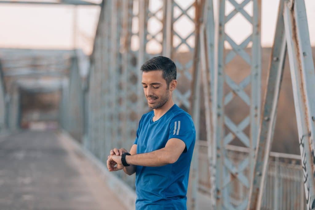 A man in a blue shirt looking at his watch while standing on a bridge