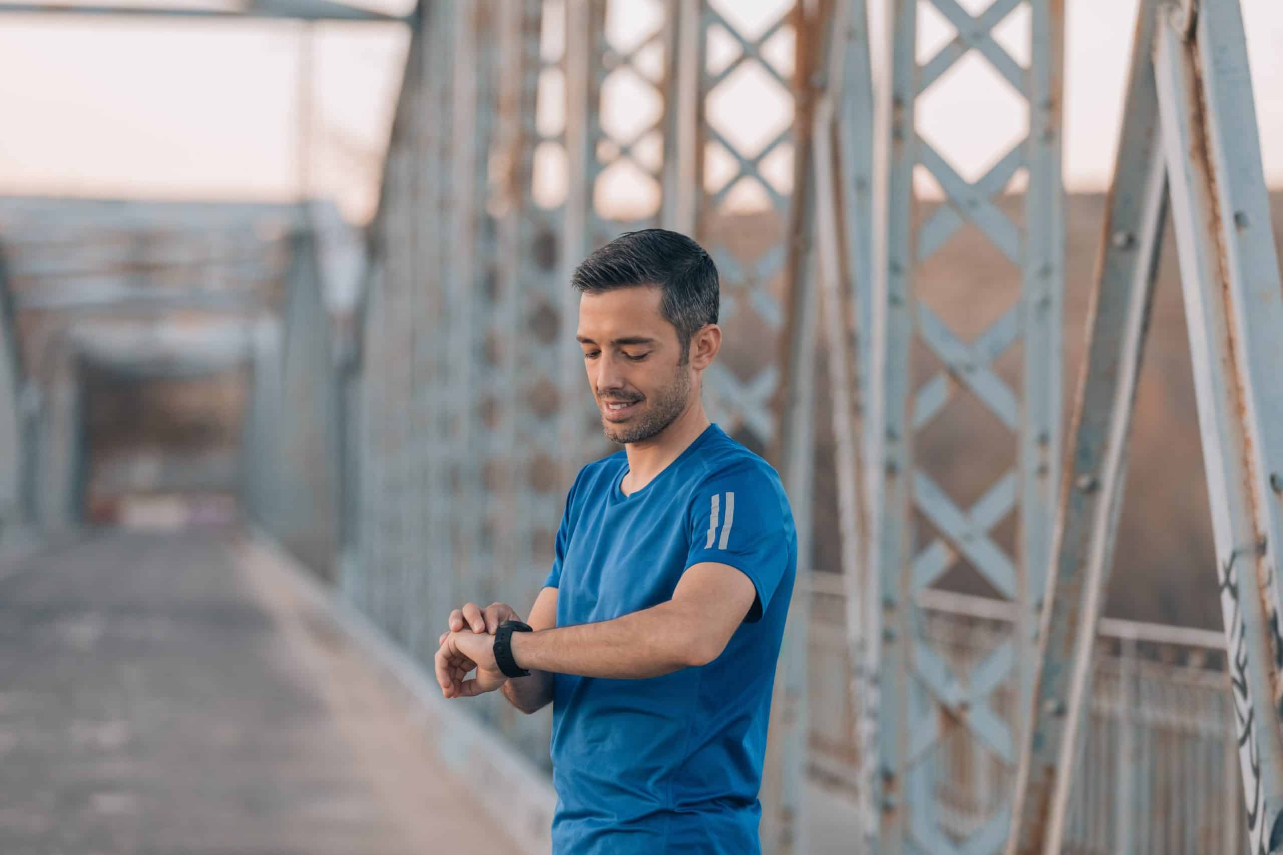 A man in a blue shirt looking at his watch while standing on a bridge