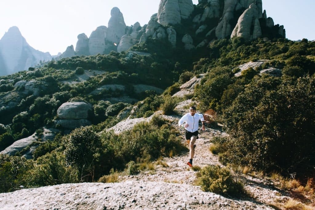 Trail runner descending a rocky mountain trail during a technical ultra-distance training run, surrounded by rugged terrain and steep rock formations
