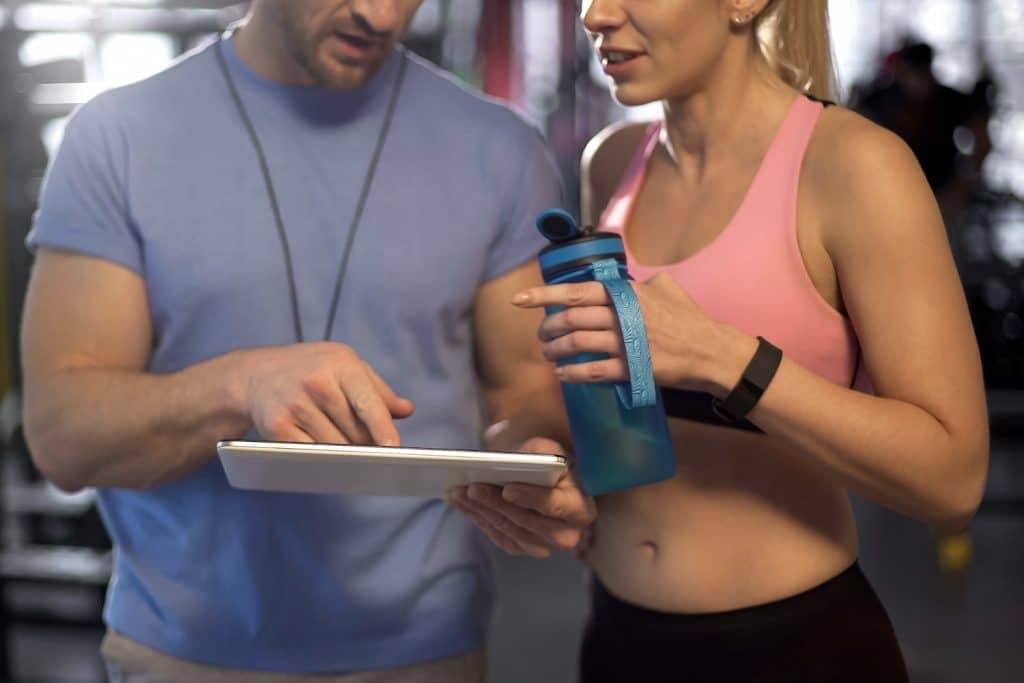 Woman in athletic apparel discussing workout program with personal trainer using a tablet