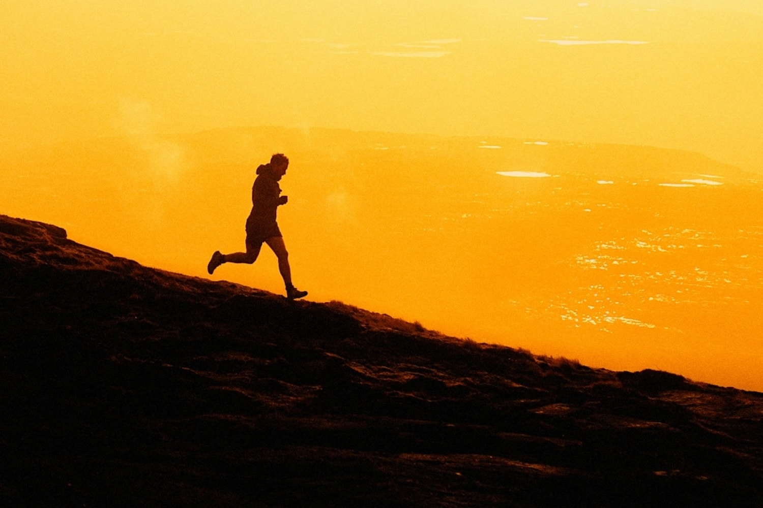 The silhouette of a person running down a hill with a yellow-gold sky in the background