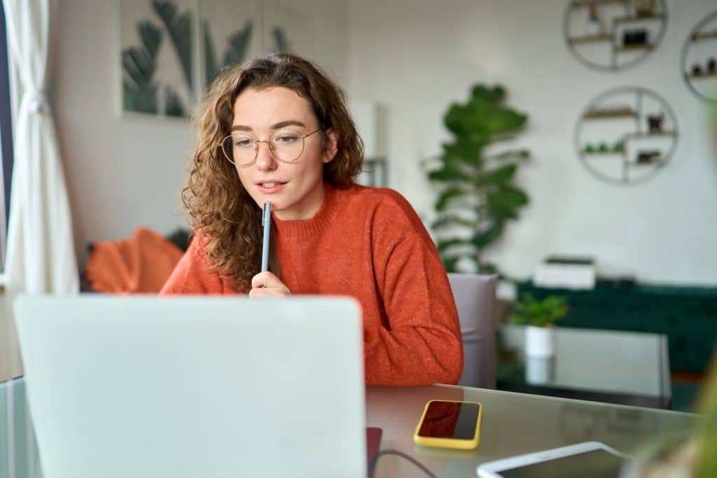 Woman on an orange sweater using a laptop at a desk