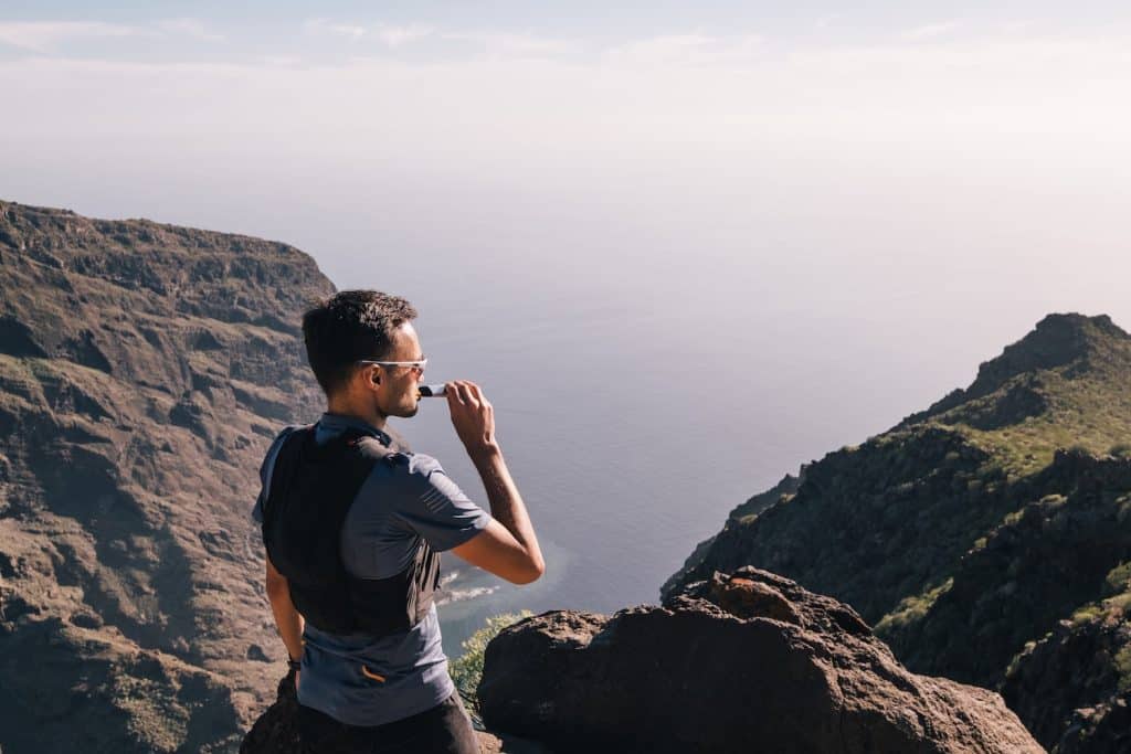 A male trail runner stopping on the top of a mountain to take in fuel