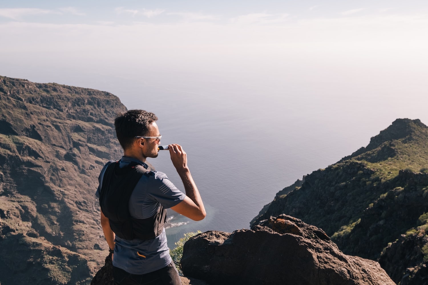 A male trail runner stopping on the top of a mountain to take in fuel