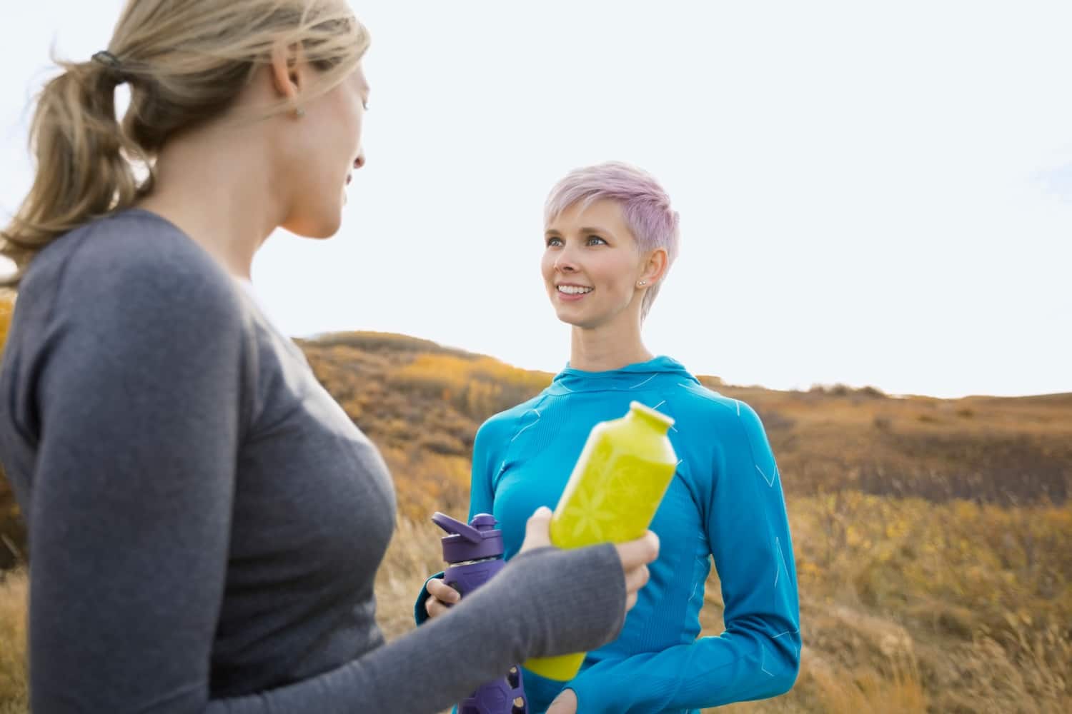 Two women holding water bottles talking outside in a field